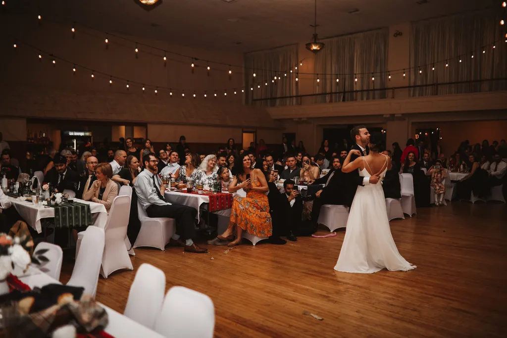 A bride dancing on the maple floor with seated guests watching from either side