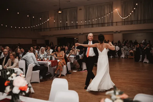 A couple dancing their first dance while guests watch from round tables in the Grand Hall