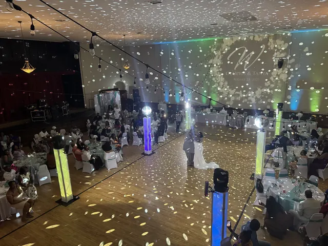 A couple sharing their first dance on the maple floor under mirror ball light and colored uplighting, seen from the balcony