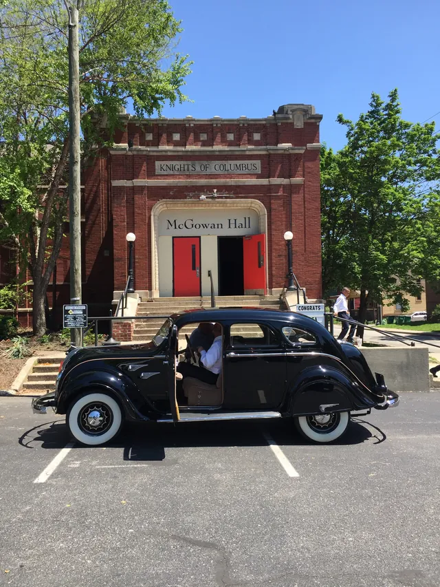 The brick front of McGowan Hall with a vintage black car parked at the steps