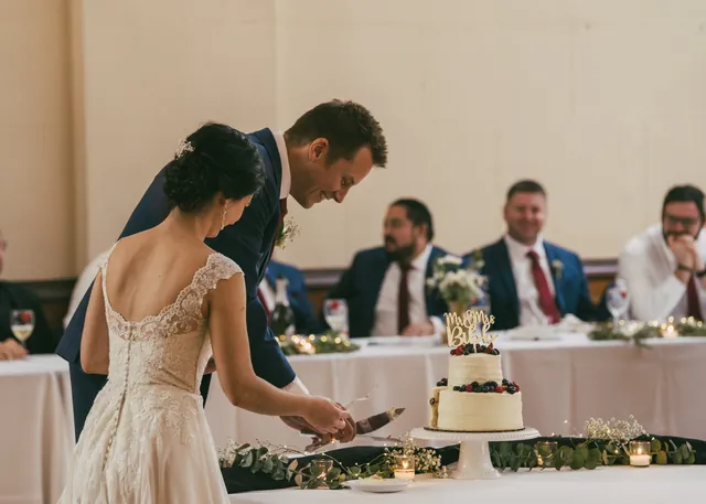 A couple cutting a naked wedding cake at the head table